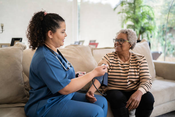 healthcare worker taking blood pressure of senior woman at home - home health nurse imagens e fotografias de stock