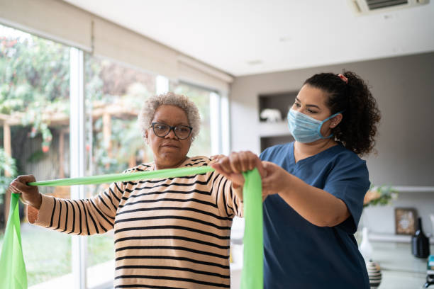 istock Senior woman doing exercise using resistance band with physical therapist support - wearing protective face mask 1334661797