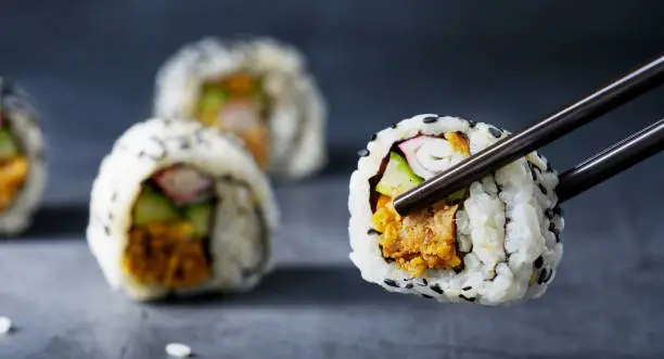 Close-up of picking up a piece of sushi with chopsticks from a black table, selective focus