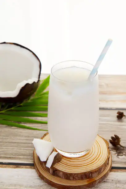 Close-up of a glass of original coconut juice on a wooden table with ice, palm leaf, natural juice, coconut shell