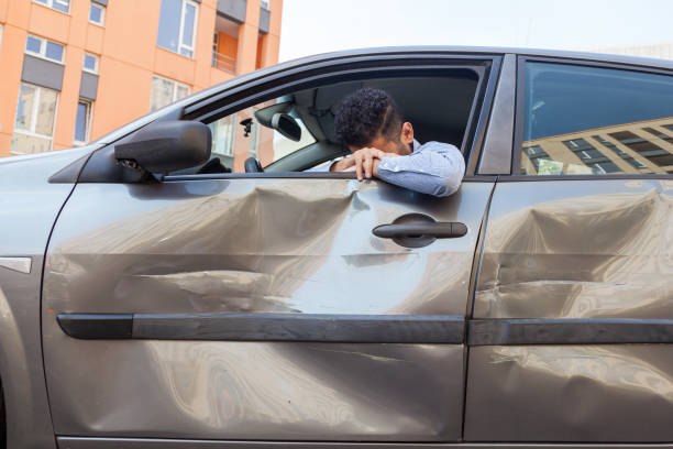 衝突した車の車輪の後ろに座っている絶望的な男は、泣きながら頭を下ろし、交通暴力、傷、自動車ドアのへこみのために車を壊しました。 - driving car traffic men ストックフォトと画像