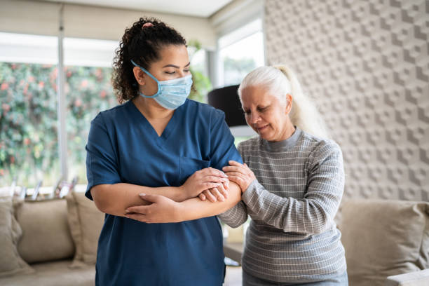 istock Home caregiver helping senior woman walking at home - wearing protecive face mask 1334662905