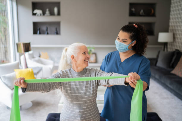 istock Senior woman doing exercise using resistance band with physical therapist support - wearing protective face mask 1334662971