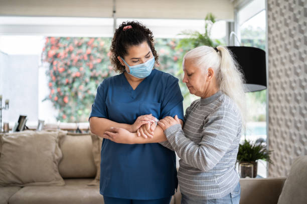 istock Home caregiver helping senior woman walking at home - wearing protecive face mask 1334662987