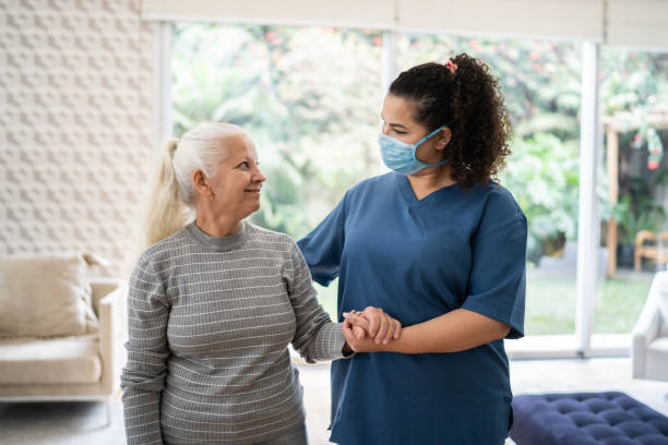 istock Home caregiver helping senior woman walking at home - wearing protecive face mask 1334663016