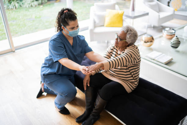 istock Physical theraphist supporting senior woman doing arm exercise at home - wearing protective face mask 1334663064