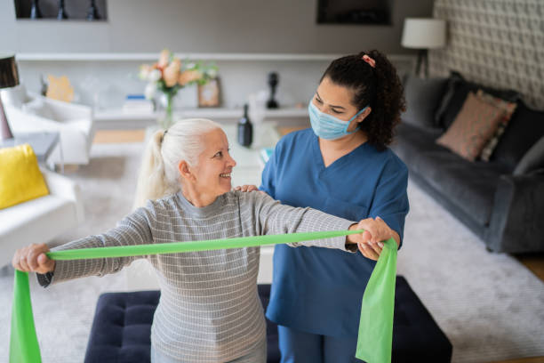 istock Senior woman doing exercise using resistance band with physical therapist support - wearing protective face mask 1334663111