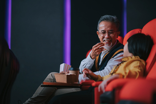Asian chinese active senior man and his granddaughter enjoy watching movie in cinema movie theatre