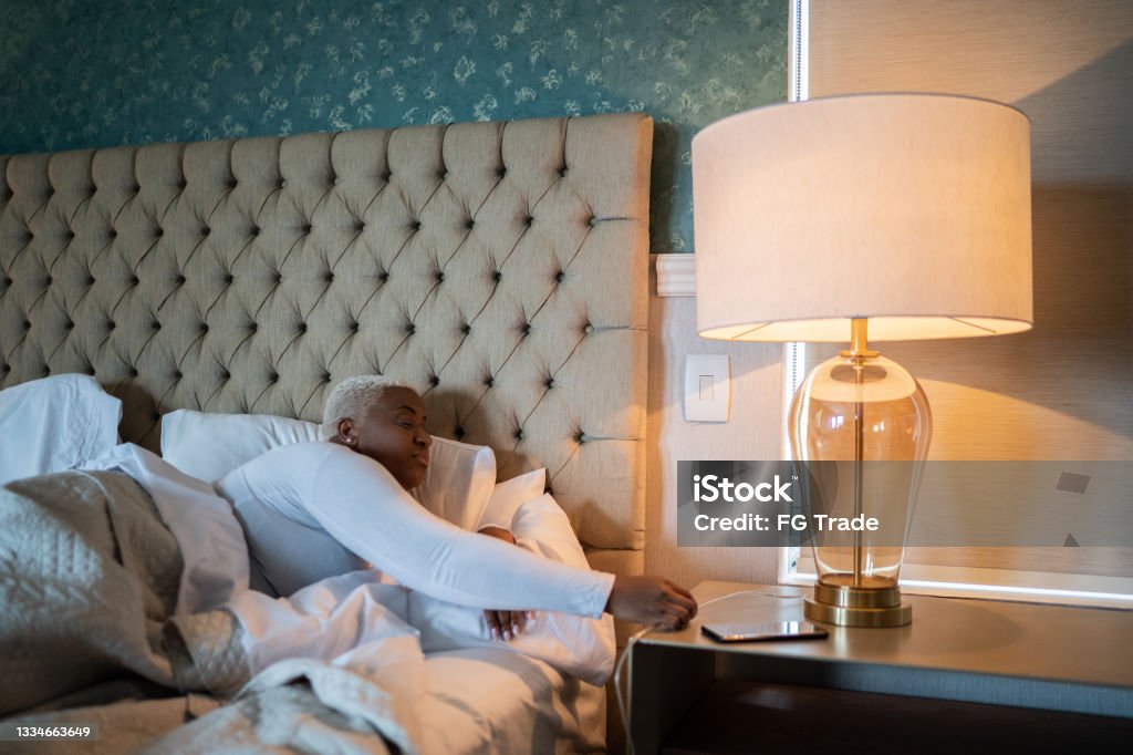 Woman going to bed and and turning off bed lamp at home Electric Lamp Stock Photo