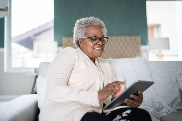 donna anziana che usa il tablet digitale a casa - ipad senior adult facebook sofa foto e immagini stock