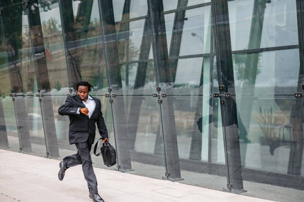 Businessman running late to work Young African-American businessman in formalwear checking the time while running to work. Time Management  for Entrepreneurs stock pictures, royalty-free photos & images