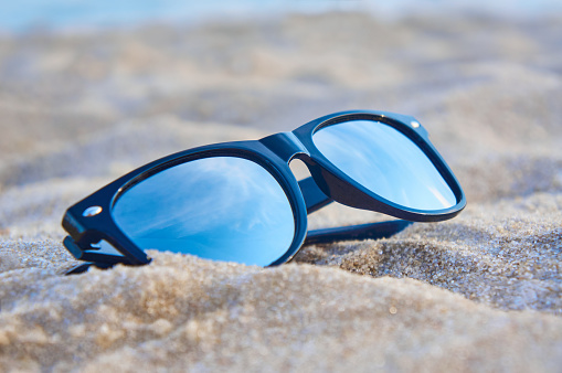 Mirror sunglasses on the sand beach with blue sky reflection