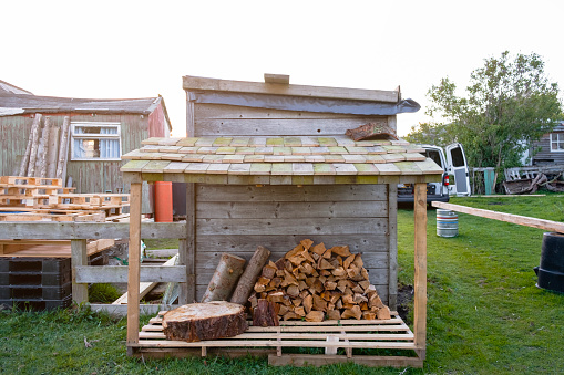 A small handmade wood store with a wood shingle roof, stocked with chopped wood and logs.