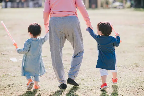 Photo of rear view low section asian chinese grandmother holding both twin baby boys grandsons hands walking in the park