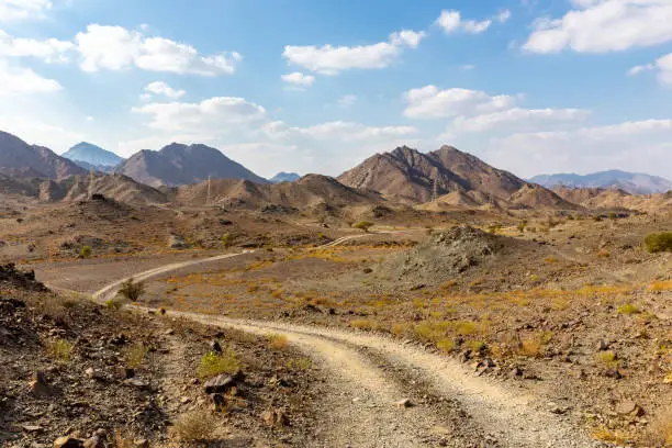 Photo of Copper Hike trail, winding gravel dirt road through Wadi Ghargur riverbed and rocky limestone Hajar Mountains, UAE.