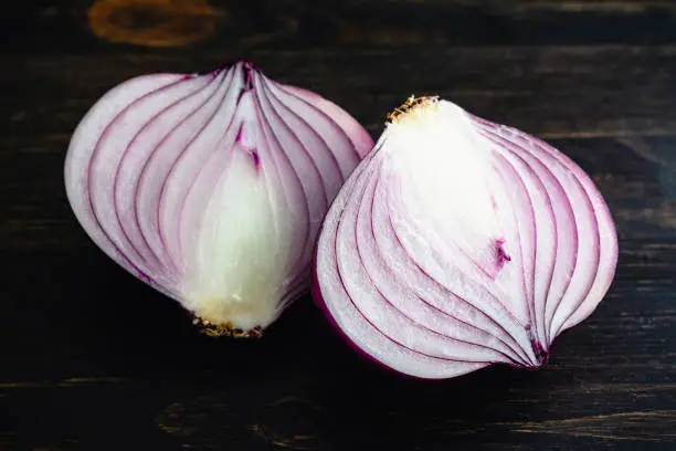 Two pieces of peeled red onion on a wooden table or cutting board