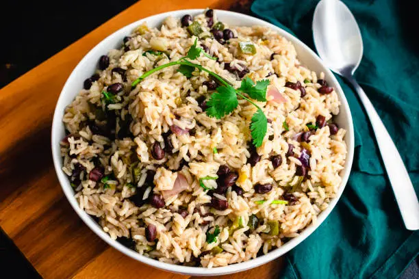 A bowl of beans and rice garnished with cilantro and shown with a serving spoon and cloth napkin