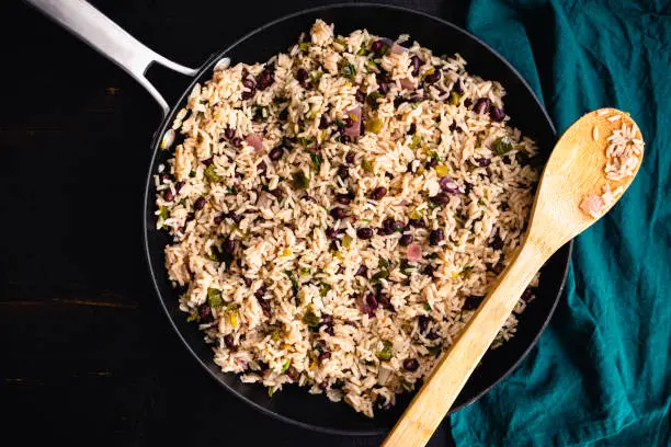 A pan of beans and rice with cilantro shown with a wooden spoon and cloth napkin