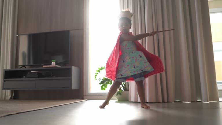 Cute girl is playing with a sword and a crown on her head at home