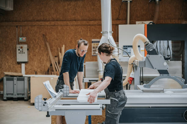 two young carpenters standing together at circular saw machine in workshop
