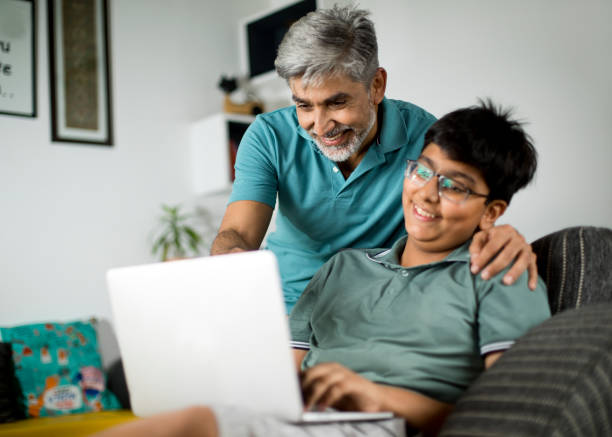 happy father and son using laptop at home - asian and indian ethnicities imagens e fotografias de stock