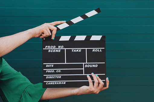 Movie production clapper board holding by female hands against green background. Cinema concept.