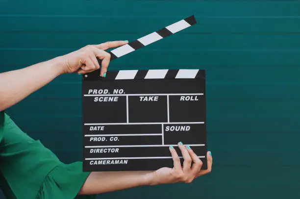 Photo of Movie production clapper board holding by female hands against green background.
