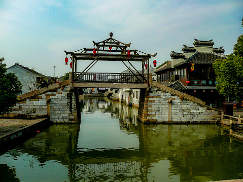 A bridge with ornate lanterns with the waters reflecting the buildings crossing the grand canal in Old Suzhou China in winter