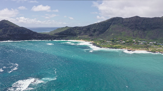 Flying drone over the ocean. View of makapuu lighthouse. Waves of Pacific Ocean wash Rocky shore. Magnificent mountains of Hawaiian island of Oahu against backdrop of blue sky with white clouds