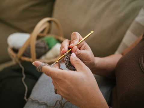 Woman sitting on sofa and doing crochet at home, hobbies and artisans concept.