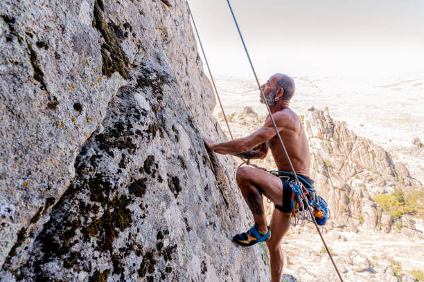 Athletic old man climbing on overhanging cliff rock