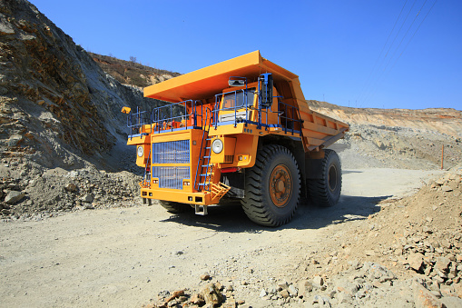 Large yellow mining dump truck on the road on a sunny day. Large-sized equipment for the transportation of rock mass in an ore quarry.