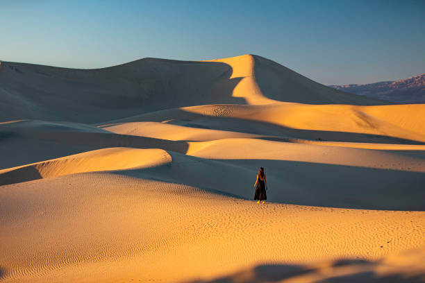 mujer vestida de pie en medio de vastas dunas de arena dorada - sand dune sand orange california fotografías e imágenes de stock