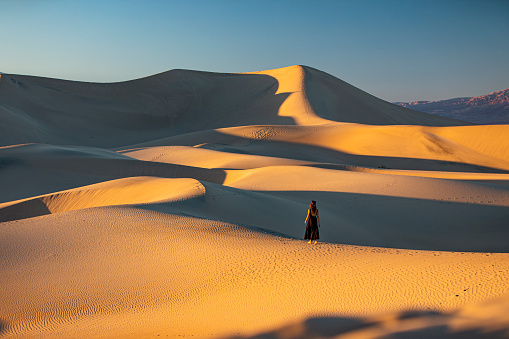 Woman in dress standing in the middle of vast golden desert sand dunes