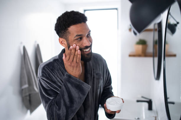 istock Young man applying cream on face indoors at home, morning or evening routine concept. 1334705480