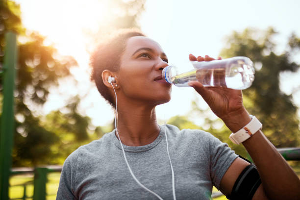 mujer afroamericana corredora bebiendo agua hidratante en la mañana - relaxation exercise audio fotografías e imágenes de stock