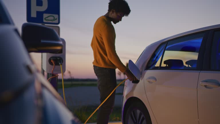 SLO MO Young man charges his electric car with blue energy at dusk