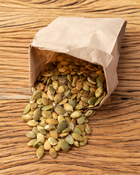 istock Pumpkin seeds in a paper bag over wooden table 1334725432