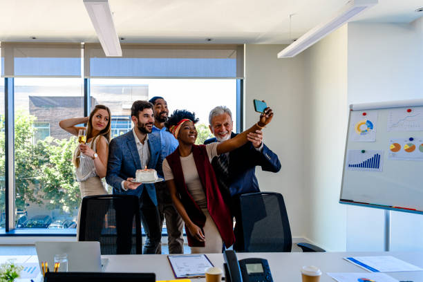 un equipo de negocios multiétnico está celebrando un cumpleaños en la oficina y fotografiando con teléfono móvil. - businessman 30s low key surprise fotografías e imágenes de stock