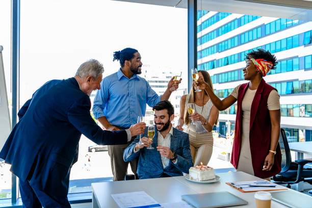 grupo de personas de negocios exitosas se divierten celebrando el cumpleaños de un colega y brindando con vino. - businessman 30s low key surprise fotografías e imágenes de stock