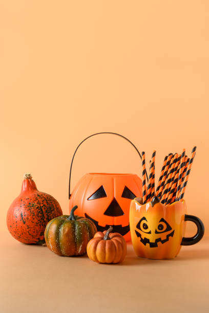 istock Halloween fun party decorations, candy bowl, pumpkins, sweets, mug with drinking straw on orange. Vertical composition. 1334735103