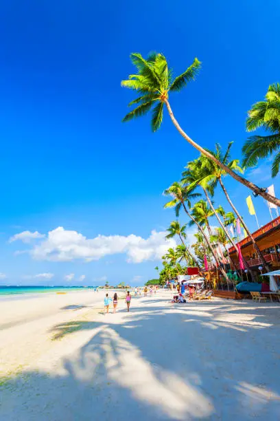 Tropical vacation at white sand beach with umbrellas, beach beds and palm trees in Boracay island in Philippines