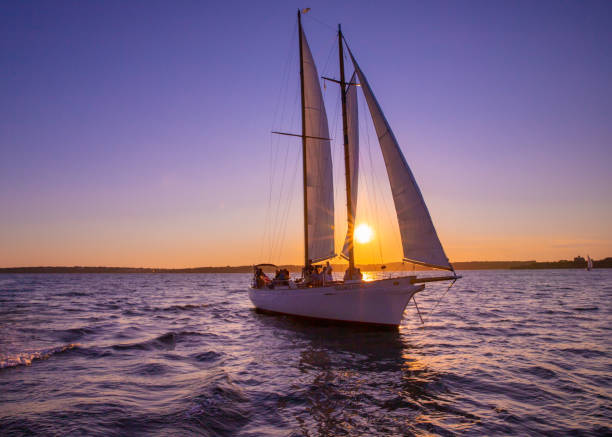 Newport, Rhode Island, USA - July 29, 2020:  Sailboat sails beneath a colorful sunset sky along the coast of Newport Rhode Island