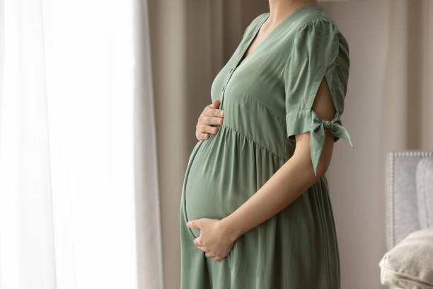 femme enceinte portant une robe pour enceinte, tenant un gros baby bump - healthcare and medicine home interior side view vertical photos et images de collection