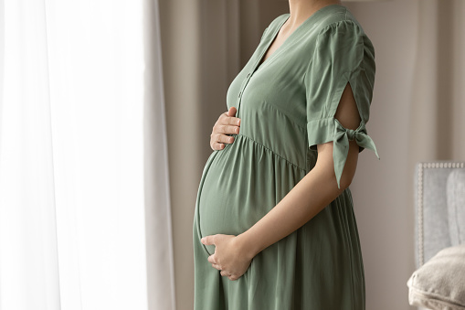 Expectant mother wearing dress for pregnant, holding big baby bump, feeling kicks, touching and hugging belly with love and care. Childbirth, pregnancy, clothes for expecting concept
