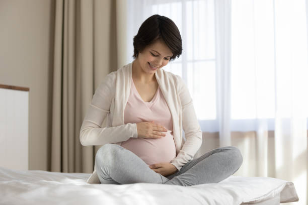 istock Happy young expectant mom sitting on bed, caressing big belly 1334740040