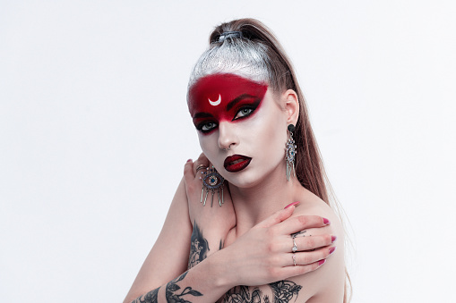 Portrait of sexy woman with long black hair and with face paint for halloween, demon woman with red face and small horns on black background. Halloween concept. Halloween Makeup