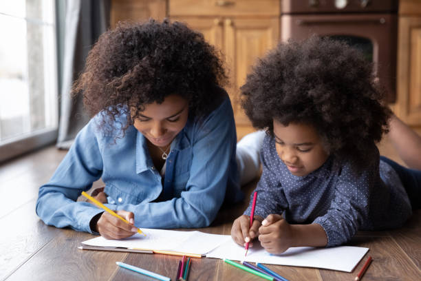 Happy biracial mom and daughter drawing in album