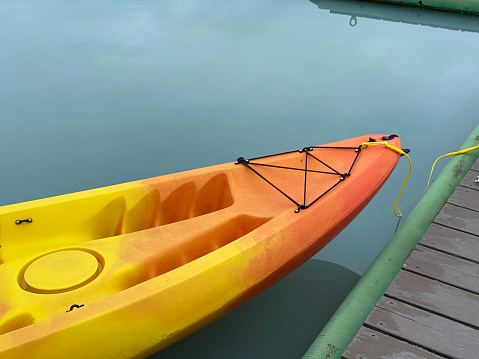 Close up of bow of orange and yellow kayak tied off on dock on calm lake with green water
