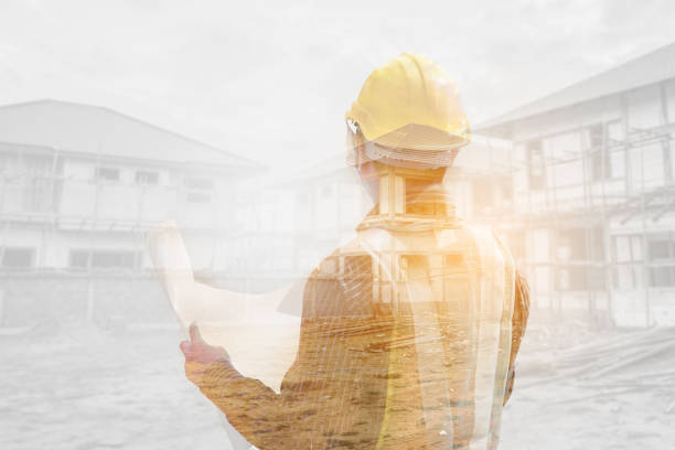 istock Double exposure image of professional engineer in protective helmet and blueprints paper at the house building construction site 1334748385